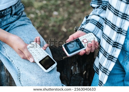 People in jeans hold push-button phones in their hands on their knees