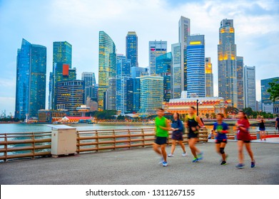 People Jogging At Singapore Embankment, Evening City Skyline In Background