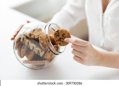 people, junk food, culinary, baking and unhealthy eating concept - close up of hands with chocolate oatmeal cookies and muesli bars in glass jar