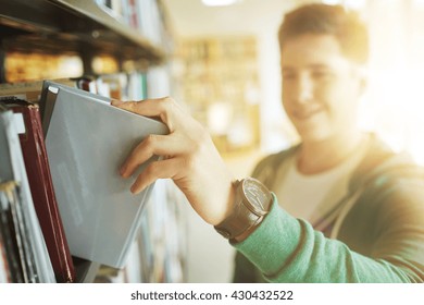 People, Knowledge, Education And School Concept - Close Up Of Happy Student Boy Or Young Man Taking Book From Shelf In Library