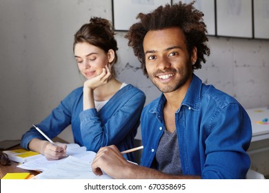 People, Learning, Knowledge And Education Concept. Candid Shot Of Handsome African American Bearded Male Student Doing Homework Together With His Attractive Caucasian Female Groupmate In Library