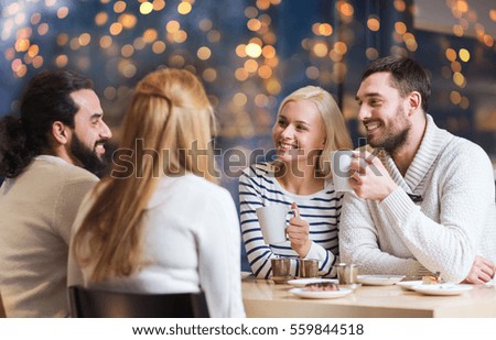 people, leisure, communication and friendship concept - happy friends meeting and drinking tea at cafe over holidays lights