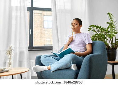 people and leisure concept - african american woman with diary and pencil sitting in chair at home and thinking