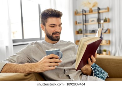 people and leisure concept - happy smiling man reading book and drinking coffee at home