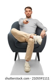 People And Leisure Concept - Man With Tv Remote Control Sitting In Chair Over White Background