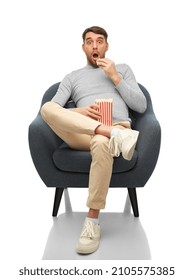 People And Leisure Concept - Surprised Man Eating Popcorn Sitting In Chair Over White Background