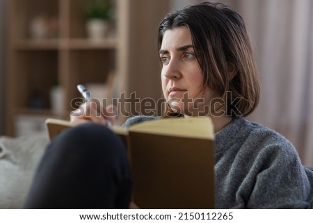 people, leisure and depression concept - sad woman with diary sitting on sofa at home