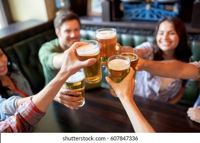 People, Leisure, Friendship And Celebration Concept - Happy Friends Drinking Draft Beer And Clinking Glasses At Bar Or Pub