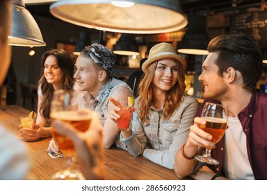 People, Leisure, Friendship And Communication Concept - Group Of Happy Smiling Friends Drinking Beer And Cocktails Talking At Bar Or Pub