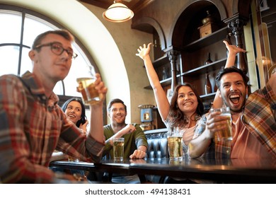 People, Leisure, Friendship And Entertainment Concept - Happy Friends Drinking Beer, Watching Sport Game Or Football Match And Celebrating Victory At Bar Or Pub