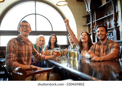 people, leisure, friendship and entertainment concept - happy friends drinking beer, watching sport game or football match and celebrating victory at bar or pub