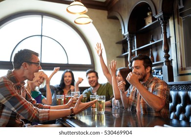 People, Leisure, Friendship And Entertainment Concept - Happy Friends Drinking Beer, Watching Sport Game Or Football Match And Celebrating Victory At Bar Or Pub