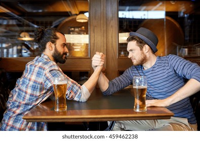 people, leisure, friendship and party concept - happy male friends drinking draft beer and arm wrestling at bar or pub and