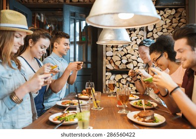 People, Leisure, Friendship, Technology And Internet Addiction Concept - Group Of Happy Smiling Friends With Smartphones Taking Picture Of Food At Bar Or Pub