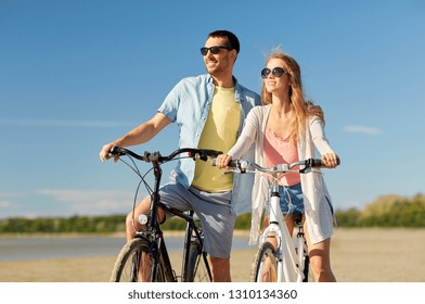 people, leisure and lifestyle concept - happy young couple riding bicycles on beach - Powered by Shutterstock