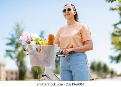 People, Leisure And Lifestyle - Happy Young Woman With Food And Flowers In Basket Of Bicycle On City Street