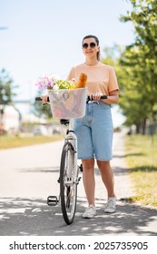 People, Leisure And Lifestyle - Happy Young Woman With Food And Flowers In Basket Of Bicycle Walking On City Street