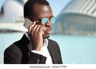 People, Lifestyle, Business And Modern Technology. Confident Afro American Businessman Wearing Black Formal Suit And Round Mirrored Lens Shades Checking Voicemail On His Way Back To Office After Lunch