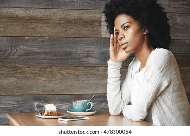 People and lifestyle concept. Cute African American female office worker, resting her elbow on table while sitting alone at coffee shop, drinking cappuccino and eating dessert during lunch break - Powered by Shutterstock