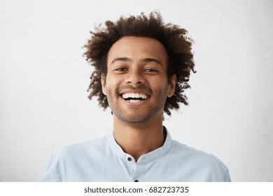People, lifestyle, happiness and positive human expressions. Studio shot of attractive young dark-skinned student with Afro hairstyle laughing at good joke, looking at camera with carefree smile