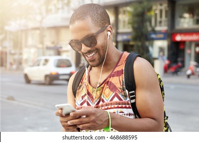 People, Lifestyle And Technology. Black College Student Having Fun And Relaxing After Hard Day At University, Walking Down Street, Listening To His Favorite Tracks And Texting Friends Using Cell Phone