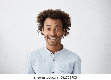People, lifestyle, youth and happiness concept. Attractive happy young dark-skinned man with stubble smiling broadly, excited with good positive news, having carefree expression on his face