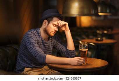 People, Loneliness, Alcohol And Lifestyle Concept - Unhappy Single Young Man In Hat Drinking Beer At Bar Or Pub