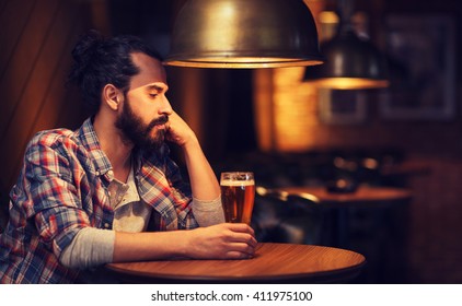 People, Loneliness, Alcohol And Lifestyle Concept - Unhappy Single Man With Beard Drinking Beer At Bar Or Pub