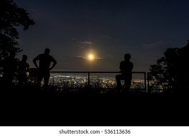 People Looking At Full Moon Raising Up In The Sky Over The City At Night