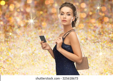 People, Luxury, Holidays And Finance Concept - Beautiful Woman In Evening Dress With Vip Card And Handbag Over Golden Lights Background