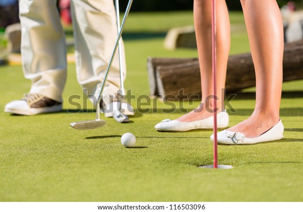 People, man and woman, only feet, playing\
miniature golf on a beautiful summer\
day