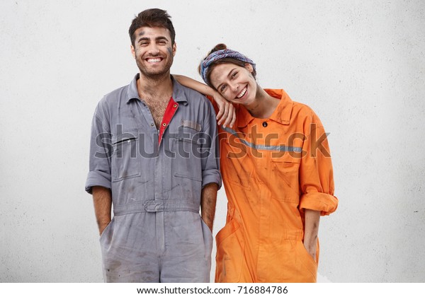 People, manual work and team work concept.\
Smiling joyful female and male professional workers, being glad to\
repair car, smile joyfully, rejoice success at work, isolated over\
white background