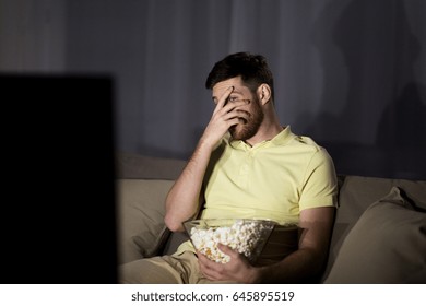 People, Mass Media, Television And Entertainment Concept - Scared Young Man Watching Tv And Eating Popcorn At Night At Home