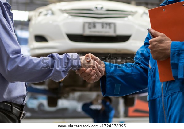 People mechanic shake hand and customer look at\
paper. service car in garage is paper checklist car. service car,\
repair, maintenance concept.Technician doing the checklist for\
repair a car.
