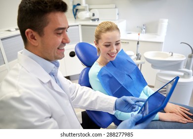 People, Medicine, Stomatology And Health Care Concept - Happy Male Dentist Showing Tablet Pc Computer To Woman Patient At Dental Clinic Office