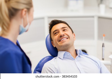 People, Medicine, Stomatology And Health Care Concept - Female Dentist Talking To Happy Male Patient At Dental Clinic Office