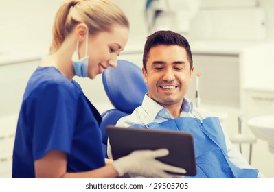 People, Medicine, Stomatology And Health Care Concept - Happy Female Dentist Showing Tablet Pc Computer To Male Patient At Dental Clinic Office