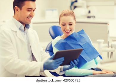 People, Medicine, Stomatology And Health Care Concept - Happy Male Dentist Showing Tablet Pc Computer To Woman Patient At Dental Clinic Office