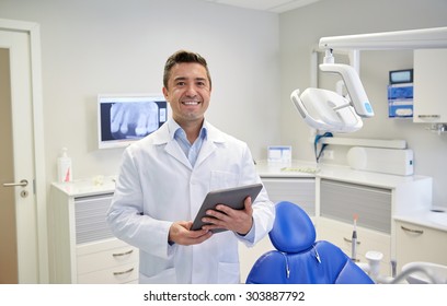 People, Medicine, Stomatology And Healthcare Concept - Happy Middle Aged Male Dentist In White Coat With Tablet Pc Computer At Dental Clinic Office