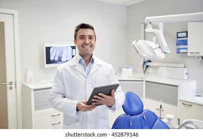 People, Medicine, Stomatology And Healthcare Concept - Happy Middle Aged Male Dentist In White Coat With Tablet Pc Computer At Dental Clinic Office