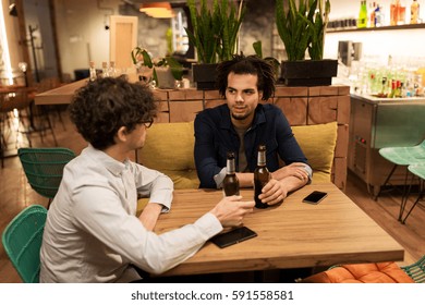 people, men, leisure, friendship and communication concept - happy male friends drinking bottled beer and talking at bar or pub