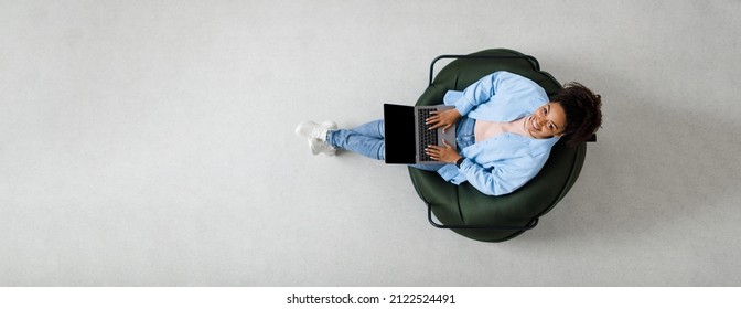 People And Modern Technology. Above Top View Of Young Smiling Black Woman Holding Pc On Lap Sitting On Bean Bag In Living Room, Looking Up At Camera. Lady Browsing Internet, Free Copy Space Panorama