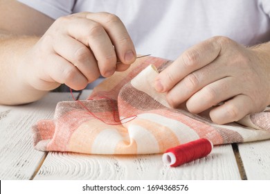 People, Needlework, Sewing And Tailoring Concept - Tailor Man With Thread In Needle Stitching Fabric. Hands Sewing With A Needle And Thread. Fingers Pulling Thread Into The Needle