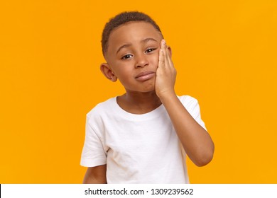 People, negative emotions, health and illness concept. Sad unhappy dark skinned male child having painful upset look, going to cry while suffering from intolerable toothache, touching chin