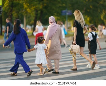 People On The Moscow City Street In Hot Summer Day. They Are Crossing The Pedestrian Cross Walk. Families With Children Of Two Different Cultures. Modern Lifestyle Concept. Backs, Rear View