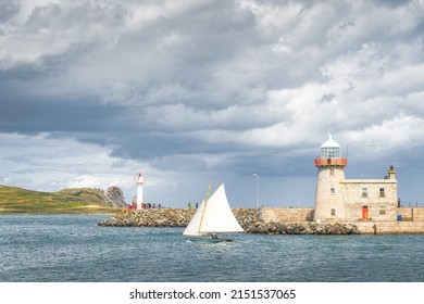 People on a small sailboat exiting Howth marina, passing Howth Lighthouse and per, with Irelands Eye island in the background, Dublin, Ireland