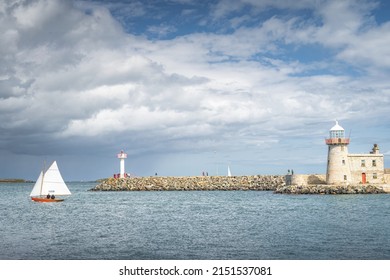 People on a small sailboat exiting Howth marina, passing Howth Lighthouse and per, Dublin, Ireland