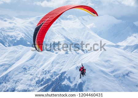 People paragliding tandem above mountain in winter in Georgia ski resort. Concept of active lifestyle and extreme sport adventure.