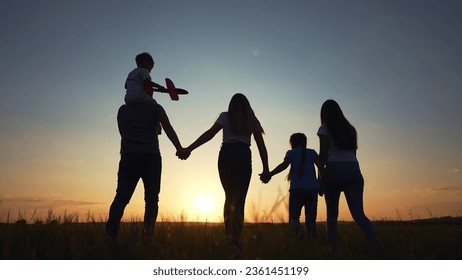 people in the park. happy family silhouette walk at sunset. mom dad and daughters walk holding hands in park. happy family kid dream concept. parents silhouette and children walking back fun - Powered by Shutterstock