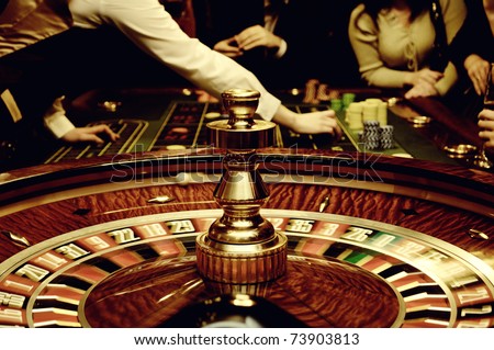 People play casino games: gold spinning roulette with motion of players, croupier (dealer) and roulette in a modern casino. Selected focus used to accent the movement and game activity.